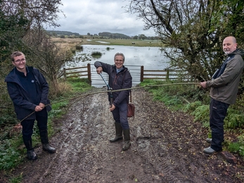 Three men in front of wetland cutting willow branch