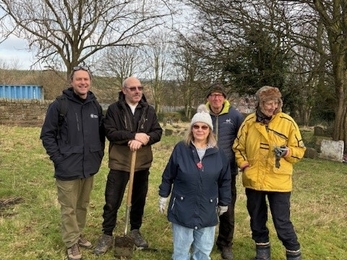 group of five people standing in greenspace with gardening tools