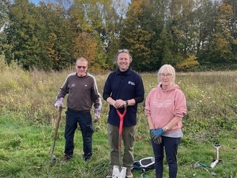 Three people posing for photo in field with gardening materials