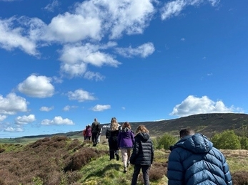 A group of young people walking up a hill in moorland, walking away from the camera