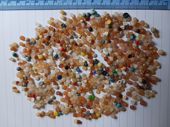 Colorful plastic pellets spread across a white surface with a blue ruler for scale.