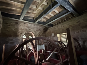 Dimly lit stone church tower with large wooden gears, exposed beams, and arched windows.