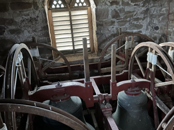 Interior of a historic bell tower with large bells, wooden frames, and stone walls.