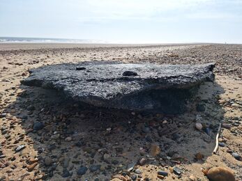 A large slab of burned nurdles on a beach, with the sea visible in the background