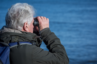 Man looking through binoculars out to sea