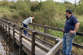 Man and woman standing on reedbed boardwalk, with wetlands either side