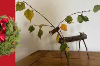 Wooden reindeer on table top next to festive wreath visual