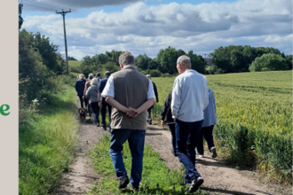 Group of people walking along track next to field with trees and clouds in distance
