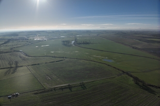 Aerial view over fields with river running through, winter sunlight in distance.