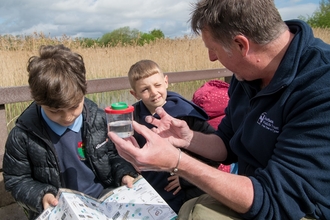 Man talking to two schoolchildren about contents of pond dipping pot