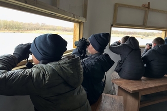 Group of young people sitting in bird hide looking out over lake