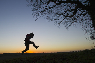 A silhouette of a child playing outdoors at sunset, The Wildlife Trusts