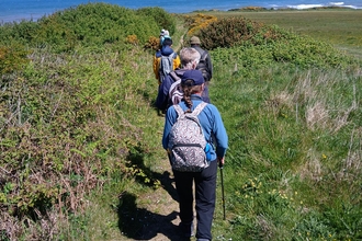 group of people walking along coastal path, with grasslands either side and sea in distance. 