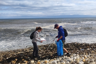 two people standing next to sea on pebble beach with litter pick equipment