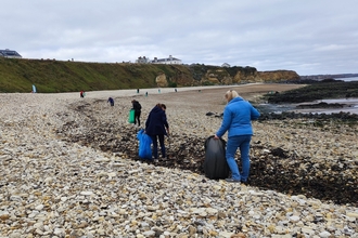 people walking on pebble beach with litter picking materials