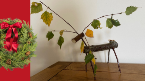 Wooden reindeer on table top next to festive wreath visual