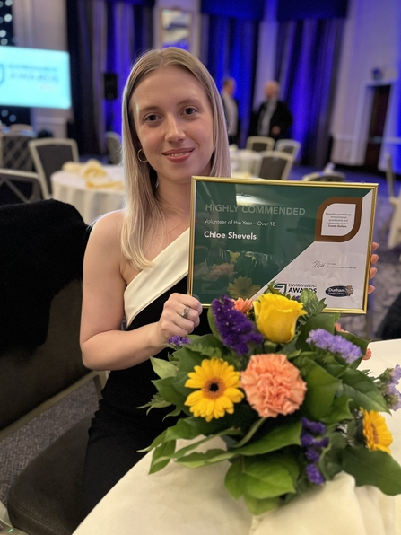 Woman holding certificate with flowers on a table in front of her