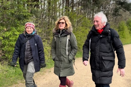 Three people walking along path next to woodland in convseration