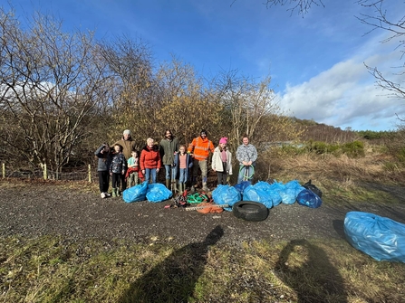 A group of people standing in front of woodland with a collection of bags full of litter