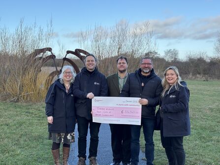 Five people stand on grass in winter clothing, holding a large ceremonial check from The National Lottery Community Fund. Behind them are leafless trees and a tall metal sculpture. The check is made out to “Durham Wildlife Trust – City of Nature, Sunderland” for £326,543, dated January 2026.