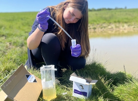 Woman next to pond with pipette and test tube from eDNA testing kit