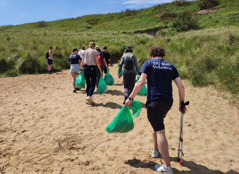group of people walking along beach with litter pick equipment